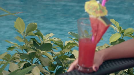 woman-on-lounge-chair-holds-glass-with-drink-near-blue-pool