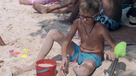 blond-boy-in-glasses-plays-with-kids-spade-and-sows-sand