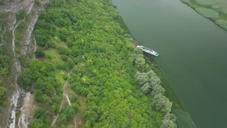 camera-with-the-turn-of-the-P-axis,-on-the-right-side,-the-river-is-visible-on-which-the-boat-A-is-moored,-on-the-left-side,-one-side-of-the-mountain-descent-with-green-trees-on-the-sides