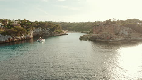 Catamaran-Boat-Floating-In-The-Calm-And-Glistening-Waters-Of-Sea-In-Cala-Llombards,-Mallorca,-Spain