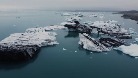 A-drone-hovers-over-a-glacier-lagoon,-its-surface-awash-with-icebergs-of-every-shape-and-size-in-Iceland