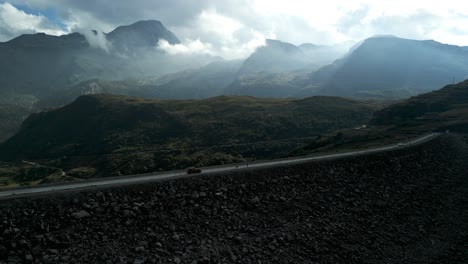 Aerial-View-Of-Car-Driving-Along-Mont-Cenis-Dam-With-Dramatic-Mountain-Landscape-In-Background