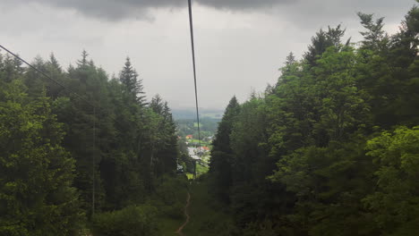 Aufsteigende-Fahrt-Mit-Der-Gondelbahn-In-Österreich-Durch-Die-Bäume-Eines-Bergresorts-Mit-Nebel-Im-Hintergrund