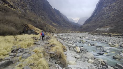 Man-trekking-besides-river-in-a-valley-between-the-mountains