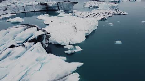 Toma-De-Drones-De-Hermosos-Icebergs-Blancos-Y-Negros-Flotando-En-Una-Laguna-En-Islandia