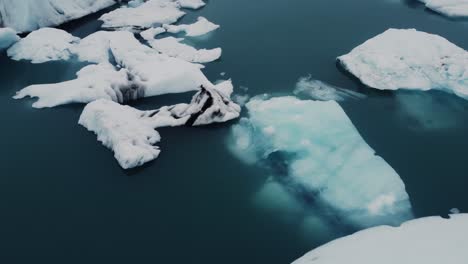 Wunderschöne-Schwarz-weiße-Eisberge,-Die-In-Einer-Lagune-In-Island-Schwimmen,-Verschwinden-Im-Blauen-Wasser