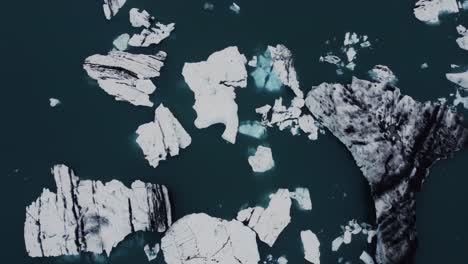 Drone-shot-of-beatiful-black-and-white-icebergs-floating-in-a-dark-blue-lagoon-in-Iceland