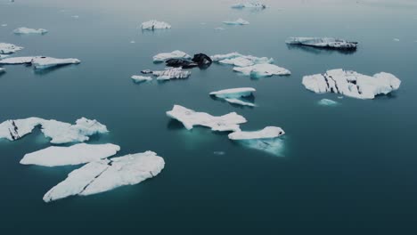 Un-Dron-Vuela-Sobre-Una-Laguna-Glaciar,-Cuya-Superficie-Es-Un-Lienzo-Para-Que-Los-Icebergs-Creen-Sus-Propias-Obras-Maestras