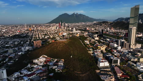 Drone-shot-circling-a-Mexican-flag-on-top-of-the-Bishopric-Hill,-in-sunny-Monterrey,-Mexico