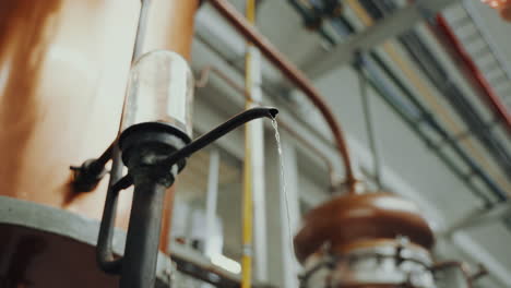 Close-up-shot-of-distilled-alcohol-coming-out-of-a-copper-tank,-industrial-process-in-a-gin-distillery-production