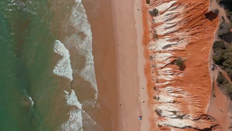Drone-top-view-of-ocean-wave-ripples-crashing-on-sandy-beach-in-algarve-portugal