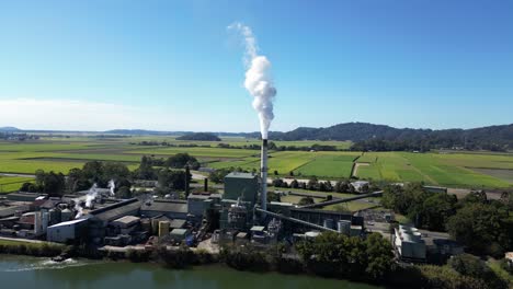 Smoke-billows-from-a-sugar-mill-refinery-on-the-banks-of-a-country-river-with-a-mountain-backdrop-view
