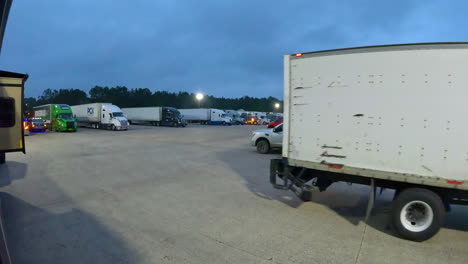 Delivery-truck-driving-through-the-large-vehicle-parking-lot-at-a-truck-stop-at-dusk