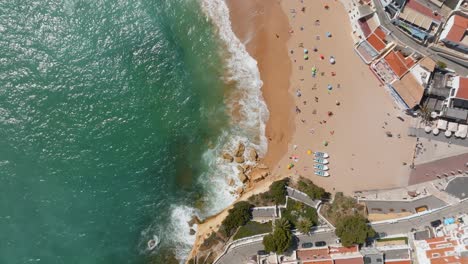 coastline-waves-crashing-on-tourists-on-beach,-carvoeiro-village,-Drone-top-down-bird's-eye-view-pan
