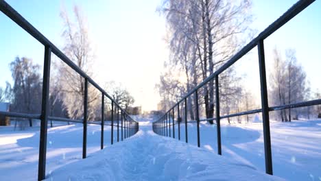 Bright-sunshine-in-sky-over-white-winter-landscape-with-small-bridge,-dolly-forward