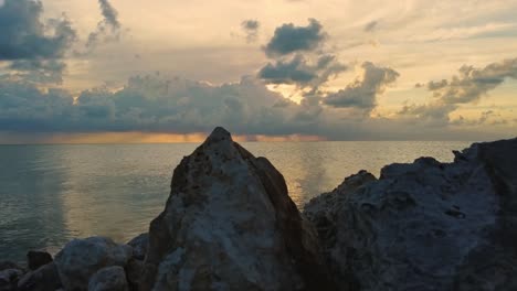 Timelapse-of-the-shoreline-rocks-in-the-foreground-and-the-clouds-and-ocean-at-dusk-near-Ambergris-Caye-or-Bay,-Belize