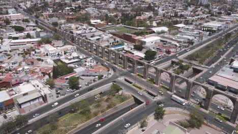 Bustling-Traffic-Flow-By-Arcos-De-Querétaro,-Ancient-Aqueduct-Monument,-Mexico