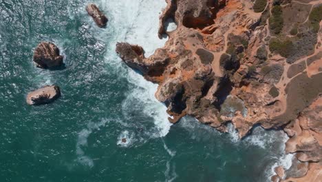 Crashing-white-waves-on-rocky-ponta-da-piedade-lagos-algarve-portugal,-Aerial-rotating-top-down