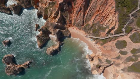 Board-walk-down-to-beach-ocean-ripples-of-ponta-da-piedade-and-praia-da-dona-ana,-drone-top-view