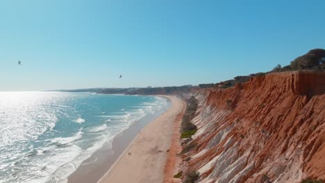 Heavily-eroded-red-white-exposde-cliffs-and-sandy-beach-stretches-in-Praia-da-Falesia,-Albufeira-Portugal