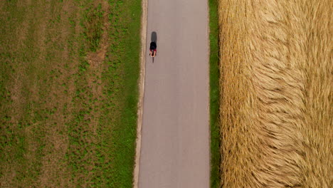 Top-down-view-of-cyclist-race-in-rural-place-with-farm-fields-of-wheat