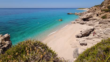 Secret-quiet-beach-hidden-by-rocks-on-Mediterranean-coastline-of-Albania,-white-sand-washed-by-crystal-emerald-water