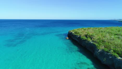 Calm-current-ripples-push-up-against-rocky-arid-cliffs,-deep-blue-caribbean-water