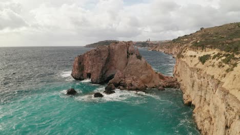 Drone-glides-close-to-Gozo's-rugged-coast-and-above-turquoise-sea-on-a-windy-day-and-reveals-ferry-departing-Mgarr-port