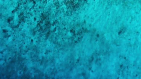 Side-to-side-view-against-ocean-ripples-currents,-top-down-drone,-clear-turquoise-water