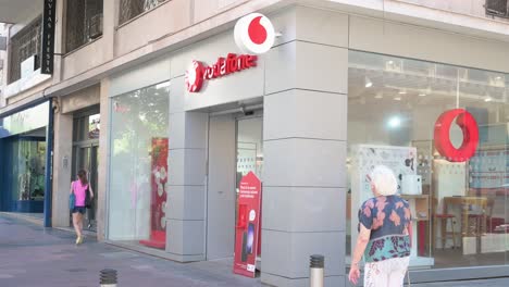 People-walk-past-the-British-multinational-telecommunications-corporation-and-phone-operator,-Vodafone,-store-in-Spain
