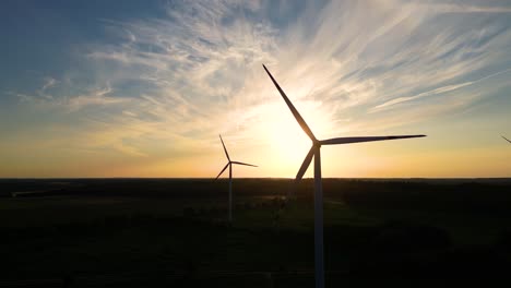 Large-wind-turbines-with-blades-in-field-aerial-view-bright-orange-sunset-blue-sky-wind-park-slow-motion-drone-turn