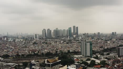 Filmische-Dorne-Aufnahme-Der-Stadtlandschaft-Von-Jakarta-Mit-Skyline-Und-Dichter-Nachbarschaft-An-Bewölkten-Tagen