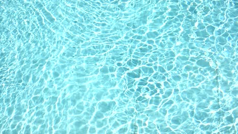 Pure-blue-water-in-the-swimming-pool-with-light-reflections-in-slow-motion.-Aerial-footage.