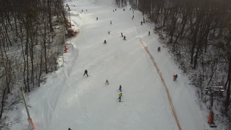 Skiers-and-snowboarders-skiing-on-snow-slopes-with-ski-lift-at-weekend.-Drone-flying-over-snowy-Slope-with-Skiers-and-Snowboarders-at-Ski-Resort-on-a-frosty-winter-day:-drone-view