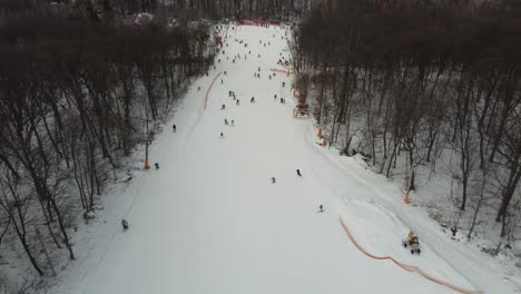 Skiers-and-snowboarders-skiing-on-snow-slopes-with-ski-lift-at-weekend.-Drone-flying-over-snowy-Slope-with-Skiers-and-Snowboarders-at-Ski-Resort-on-a-frosty-winter-day:-drone-view
