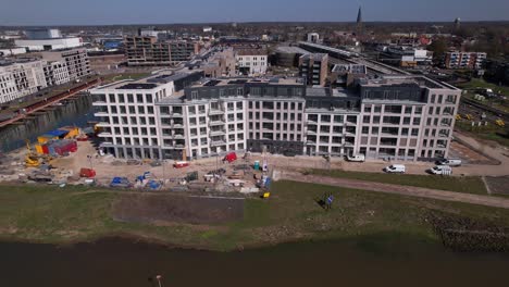 Aerial-descend-revealing-facade-and-construction-site-of-luxury-Kade-Zuid-apartment-complex-at-riverbank-of-river-IJssel-between-train-tracks-and-recreational-port