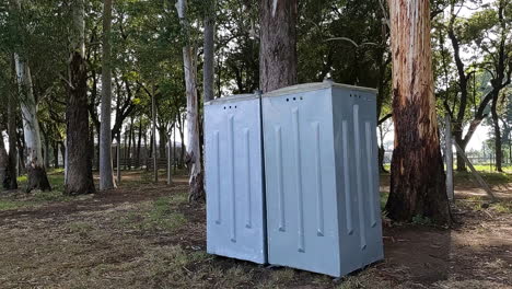 Close-up-shot-of-grey-outdoors-portable-bathroom-surrounded-by-forest-of-eucalyptus-trees,-It's-sunny-outside