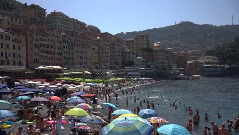Tourists-enjoy-the-relaxing-atmosphere-and-engage-in-sunbathing,-where-they-lay-out-on-the-sandy-shores,-soaking-in-the-warm-Mediterranean-sun-against-the-charming,-colourful-houses-in-Camogli,-Italy
