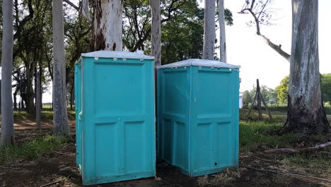 dolly-forward-of-two-aqua-green-blue-portable-bathrooms-in-family-park-with-trees