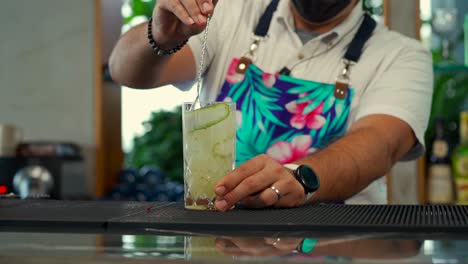 Lateinamerikanisch-mexikanische-Barkeeper-Zeigen-Flair-Routine-Bei-Der-Zubereitung-Frischer-Getränke-Im-Strandrestaurant-Mit-Gurke-Und-Zitronengarnitur,-Rotem-Side-Shot-Tequila-Sunrise-Mojito-Gin-Mezcal