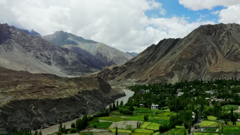 Cámara-Aérea-De-Drones-Moviéndose-Sobre-Leh-Ladakh-Con-Vegetación-En-Un-Lado-Y-Montañas-En-El-Otro-Lado-Con-Una-Corriente-Fresca-Que-Fluye-En-El-Medio