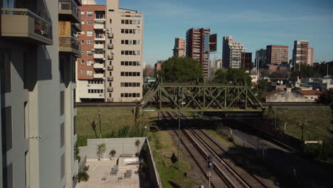 Red-train-passes-over-the-bridge-in-the-city,-summer,-Buenos-Aires
