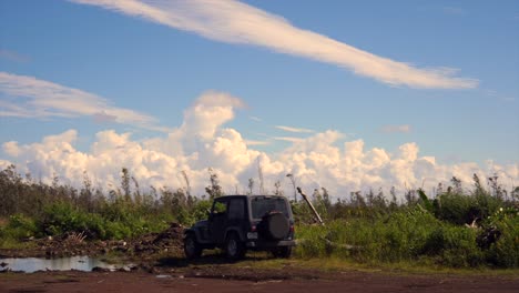 Black-jeep-parked-on-volcanic-land-with-forest-regrowth-and-impressive-cloud-formations