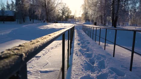 Deep-foot-prints-on-snow-over-steel-old-bridge,-majestic-winter-sunset-and-snowfall