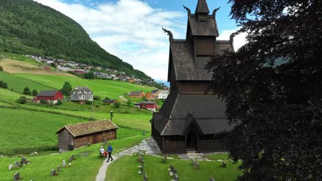 Hopperstad-Stave-Church-exterior-aerial-during-summer---Church-seen-behind-tree-with-mountain-background---Norway-60-fps