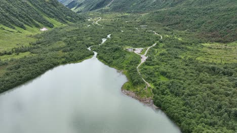 Aerial-descending-towards-Brevatnet-glacial-lake-with-glacier-runoff-water-from-Boyabreen-in-Fjaerland-Norway---Lush-green-valley-with-river-and-turquoise-lake-in-60-fps---Tourists-standing-on-beach