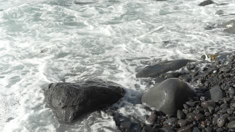 Close-up-of-wave-rolling-in-on-black-rocky-stone-beach