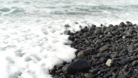 Calm-wave-rolls-in-on-black-glistening-pebble-beach,-Tenerife