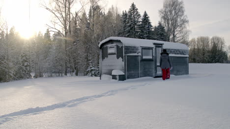A-warmly-dressed-woman-walks-through-the-snow-to-a-hut-and-tries-to-open-the-door