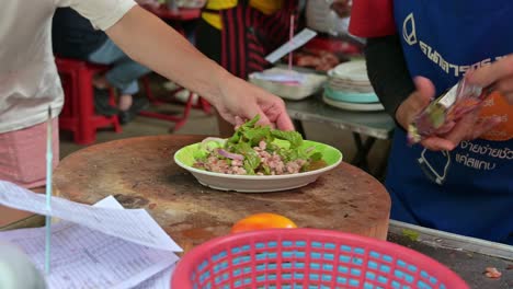 Street-hawkers-serving-a-plateful-of-Laab,-a-famous-street-food-originally-from-the-Northeastern-Thailand-of-the-Isan-region